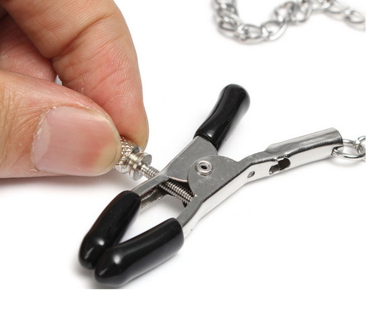 A classic black solid ball gag with an adjustable faux-leather strap and two integrated metal alligator nipple clamps on silver chains.